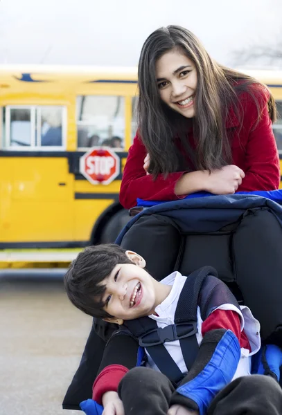 Sorella maggiore con fratello disabile in sedia a rotelle con scuolabus — Foto Stock