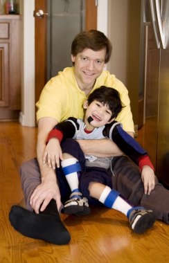 Father holding disabled son on kitchen floor clipart