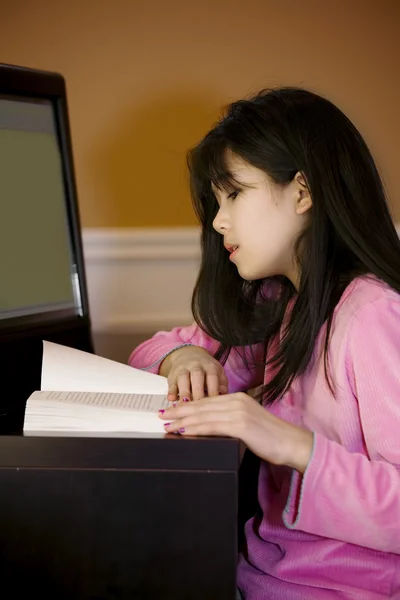 Десять летняя азиатка читает за столом, за компьютером — стоковое фото