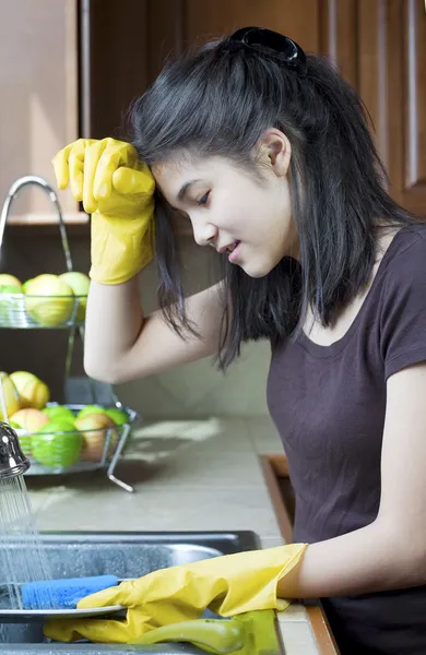 Teen girl washing dishes at kitchen sink, tired expression. — Stock Photo, Image