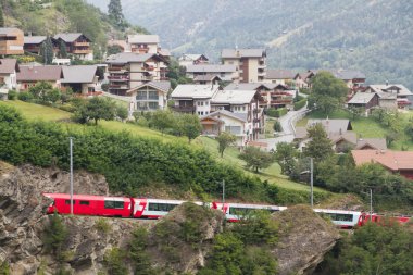 Glacier express train passes village, Switzerland clipart