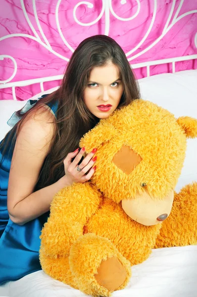 Schöne Frau sitzt auf einem Bett mit Teddybär — Stockfoto