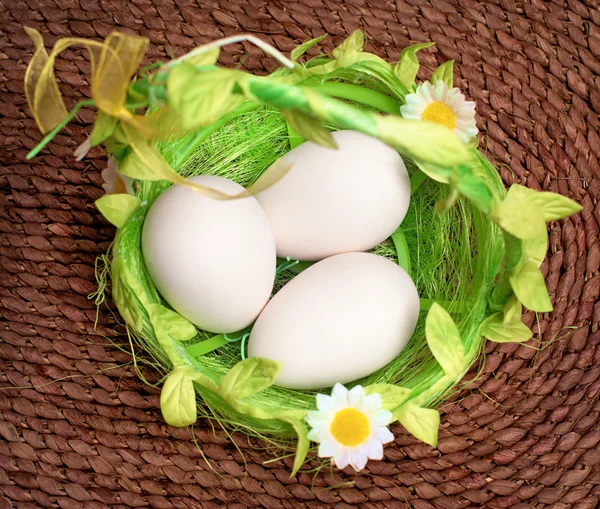 Яйца в зеленой корзине на плетеном фоне — стоковое фото