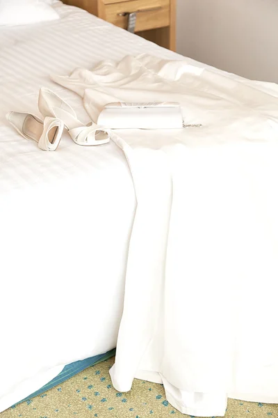 Svatební šaty, boty a tašku na postel — Stock fotografie