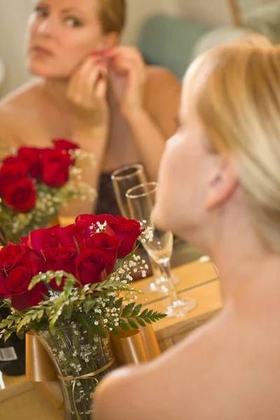Mujer rubia aplica maquillaje en el espejo cerca de champán y rosas —  Fotos de Stock