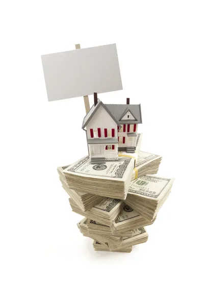 Casa pequena em pilhas de notas de cem dólares e sinal em branco — Fotografia de Stock