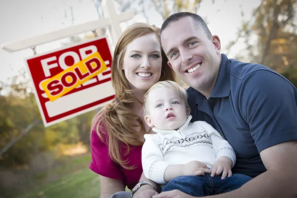 Familia joven feliz en frente de la venta de bienes raíces — Foto de Stock