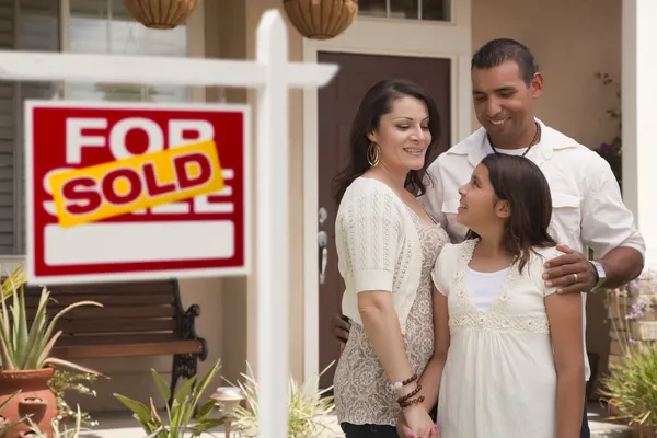 Familia hispana frente a casa con letrero inmobiliario vendido —  Fotos de Stock