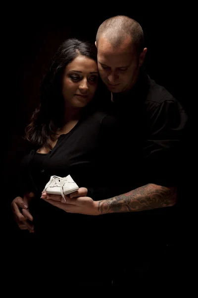 Casal de corrida mista segurando novos sapatos de bebê branco no preto — Fotografia de Stock