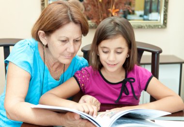 Hispanic grandmother rading with her granddaughter at home clipart