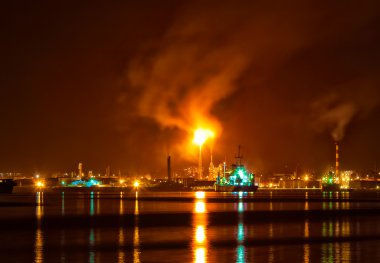 Oil refinery at night with a huge smoke column polluting the air clipart