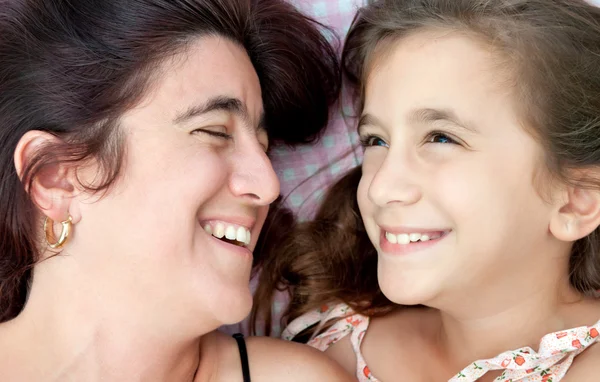 Genç latin anne ile kızı yatakta döşeme ve gülüyor — Stok fotoğraf