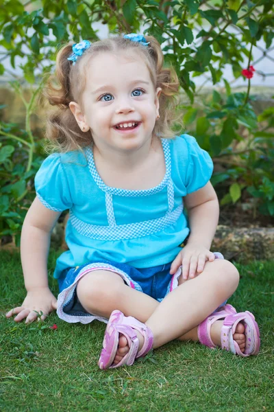 Mooie kleine blonde meisje, zittend op het gras — Stockfoto