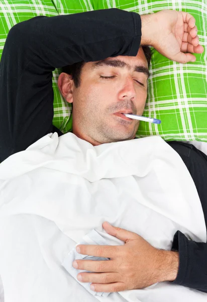 Hombre hispano enfermo acostado en la cama con un termómetro — Foto de Stock