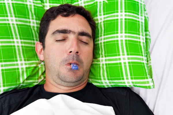 Uomo ispanico malato sdraiato a letto con un termometro — Foto Stock