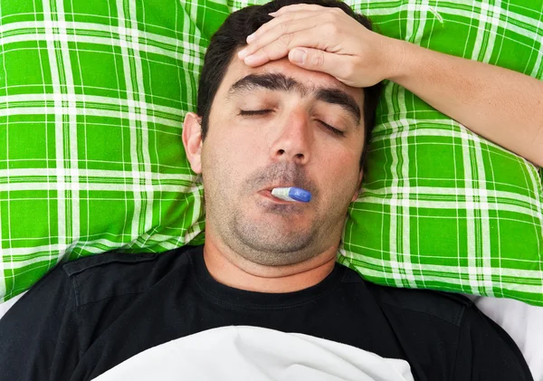 Хворий іспаномовний чоловік лежить у ліжку з гарячкою — стокове фото