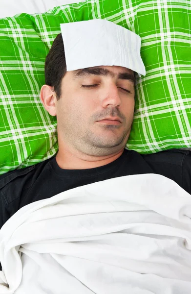 Zieke man in bed met een tissue in zijn voorhoofd — Stockfoto