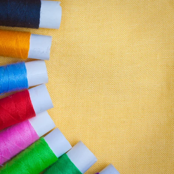 Carretes de hilo de coser sobre un fondo de tela amarilla — Foto de Stock
