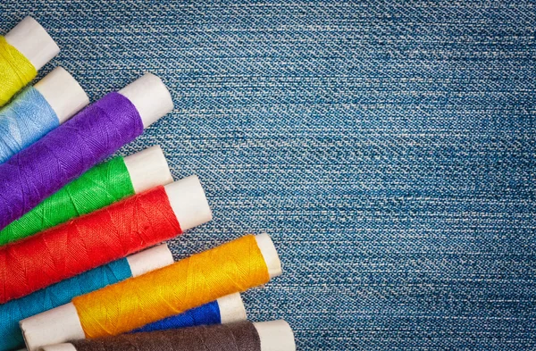 Sewing thread reels on a blue denim background — Stock Photo, Image