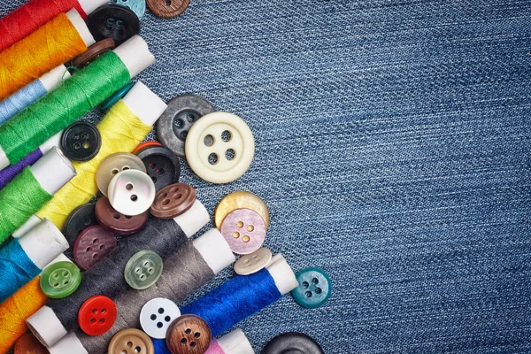 Botões de costura e bobinas de linha em um fundo de ganga — Fotografia de Stock