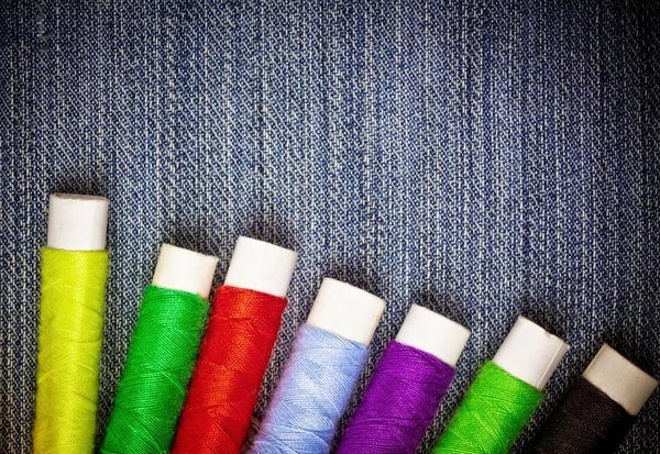 Carretes de hilo de coser sobre un fondo de mezclilla azul — Foto de Stock