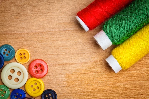 Sewing buttons and thread reels on a wood background — Stock Photo, Image