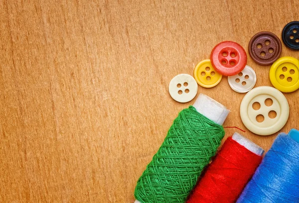 Sewing buttons and thread reels on a wood background — Stock Photo, Image