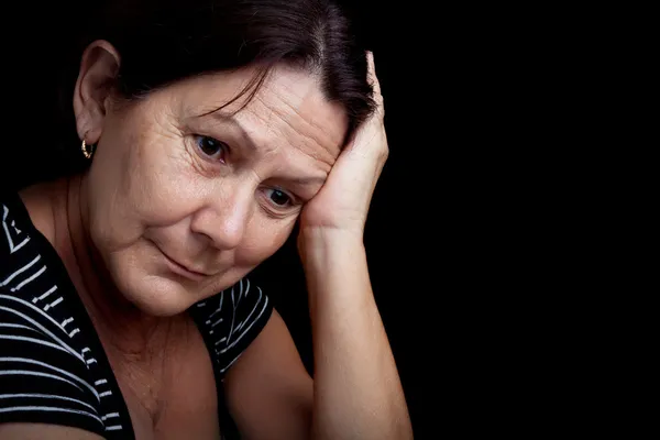 Ältere Frau mit sehr traurigem Gesichtsausdruck, isoliert auf schwarz Stockbild