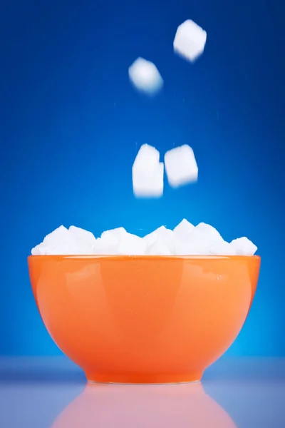 Cubos de açúcar caindo em uma tigela de laranja — Fotografia de Stock