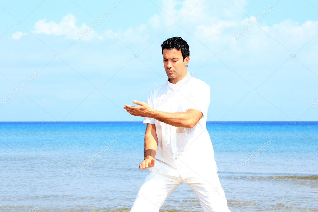 Handsome man practicing thai chi on the beach