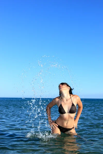 Menina bonito na praia espirrando para fora da água — Fotografia de Stock