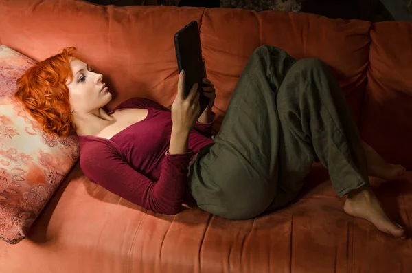 Lockige Frau auf einem Sofa mit eBook lizenzfreie Stockfotos