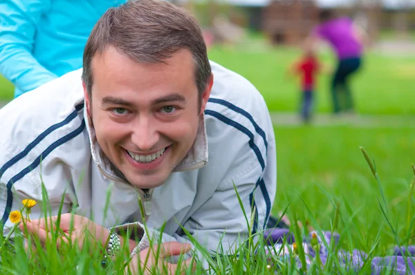 Mladý otec ležel v trávě na slunný jarní den s úsměvem — Stock fotografie