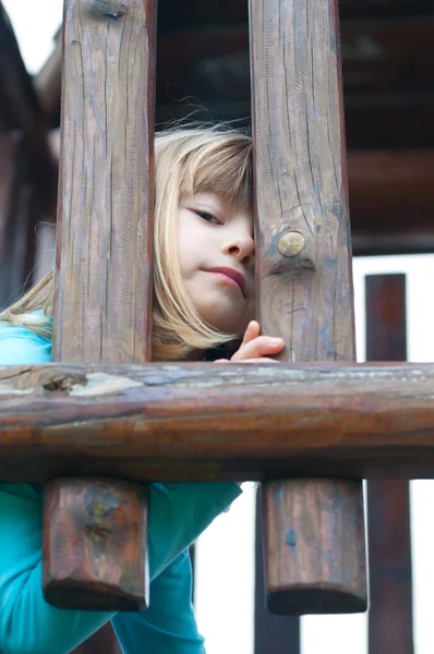 Милая маленькая девочка, выглядывающая через деревянные решетки — стоковое фото