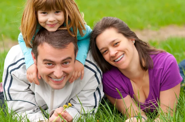 Jovem família feliz se divertindo na grama no belo dia de primavera — Fotografia de Stock