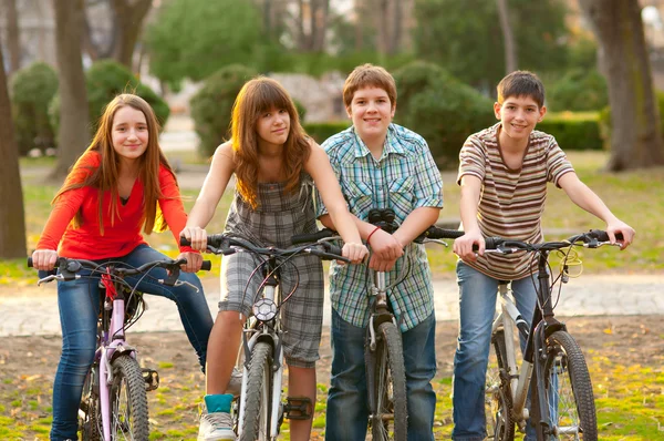 Fyra glada tonåriga vänner ridning cyklar i parken — Stockfoto