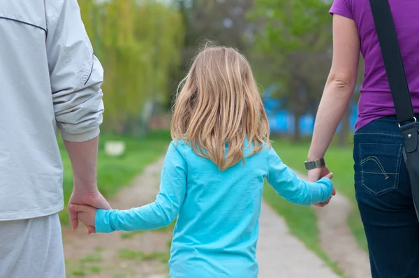 少女が公園で歩いている間彼女の両親の手を繋いでいます。 — ストック写真
