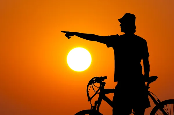 Σιλουέτα του αναβάτη ποδήλατο ήλιο και πορτοκαλί ουρανό δείχνει κάτι στο βάθος — Φωτογραφία Αρχείου
