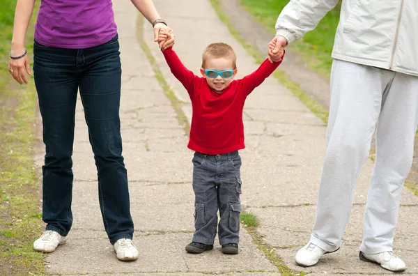 少年が公園を歩いている間彼の両親の手を繋いでいます。. — ストック写真