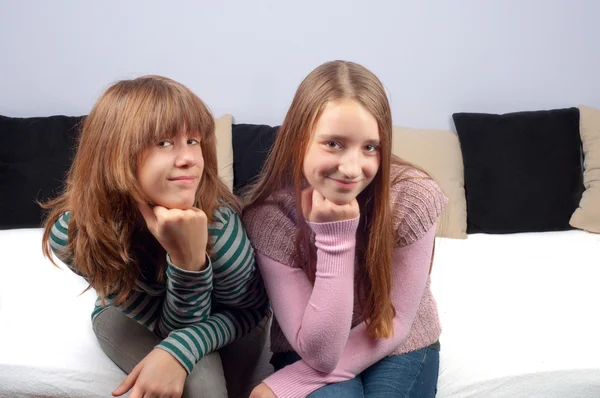 Две симпатичные девочки-подростки сидят на кровати и улыбаются — стоковое фото