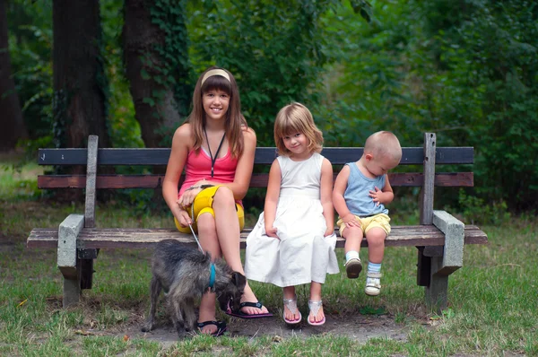 Tonårig flicka sitter med sin mycket yngre bror och syster i parken — Stockfoto
