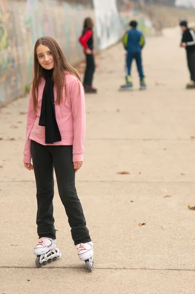 Bastante sonriente chica en rodillos posando fuera con amigos en el backgroun —  Fotos de Stock