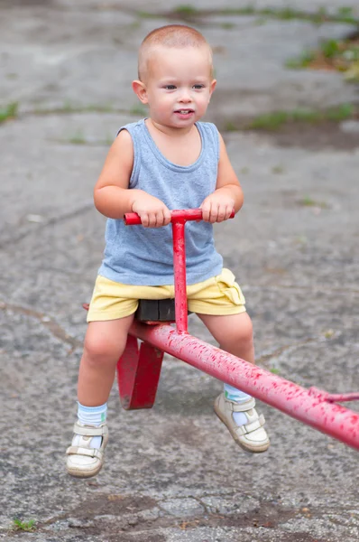 Lächelnder Junge sitzt an bewölkten Sommertagen auf dem Spielplatz — Stockfoto