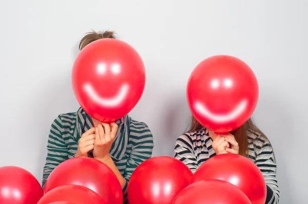 Teenage girls hiding their faces behind smiling balloons — Stock Photo, Image