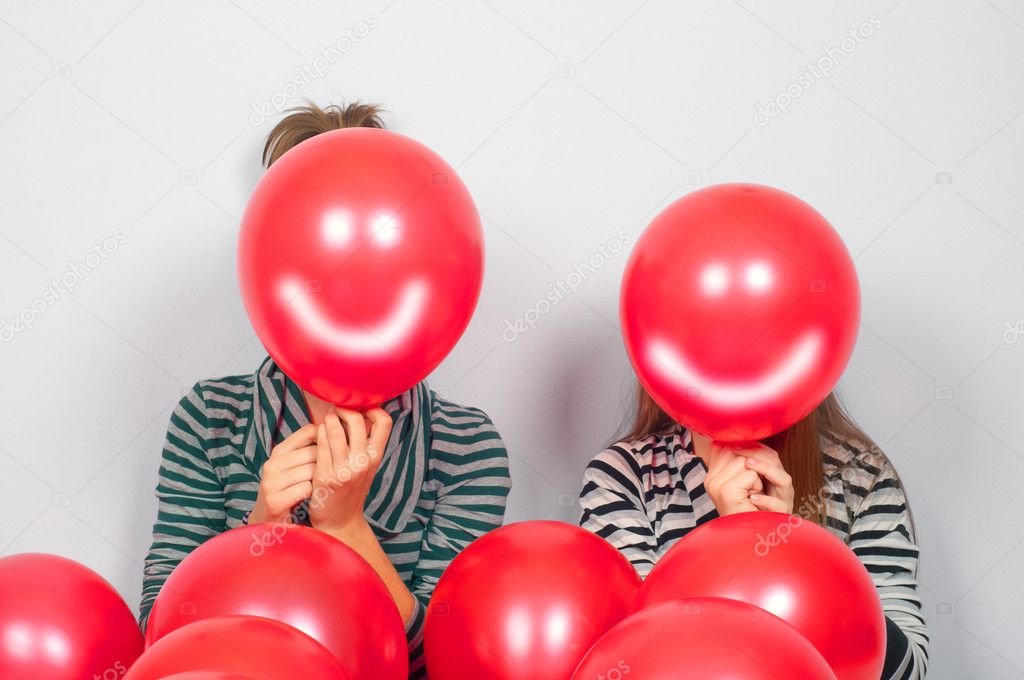 Teenage girls hiding their faces behind smiling balloons
