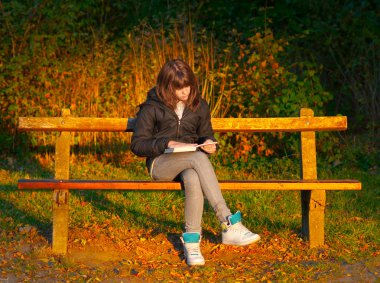 güzel genç kız bankta otururken kitap okur.