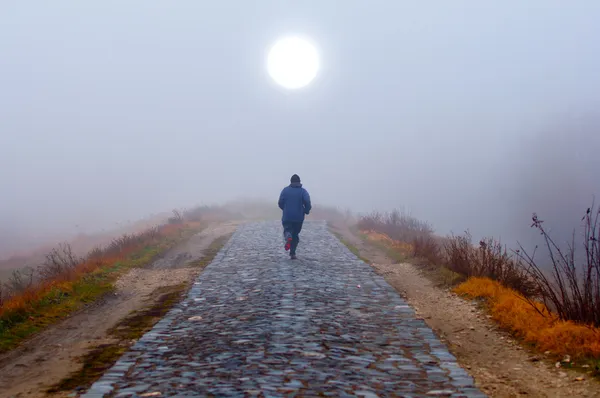 Одинокий человек бежит к солнцу туманным осенним утром — стоковое фото