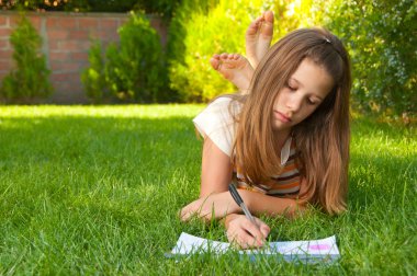 Cute teenage girl lies on the grass and draws in her notebook