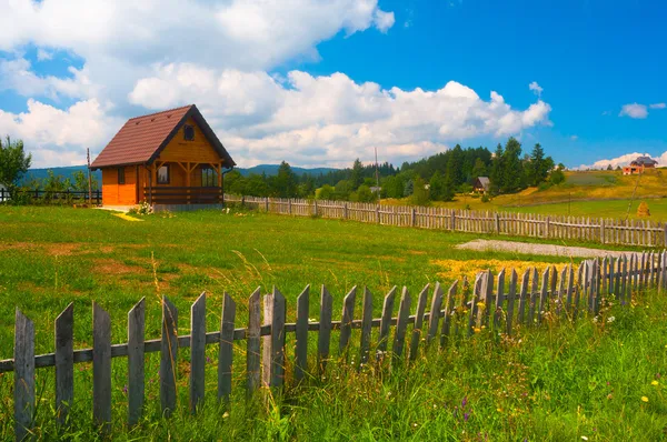 Заміський пейзаж, що показує маленький будинок, луг і дерев'яний паркан — стокове фото