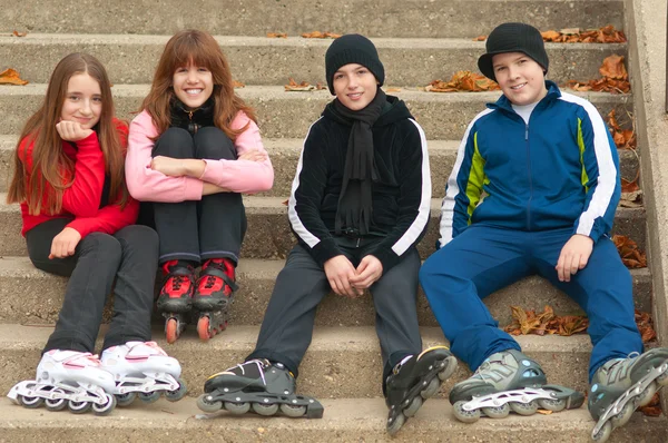 Group of happy teenagers in roller skates sitting on the stairs — Stock Photo, Image